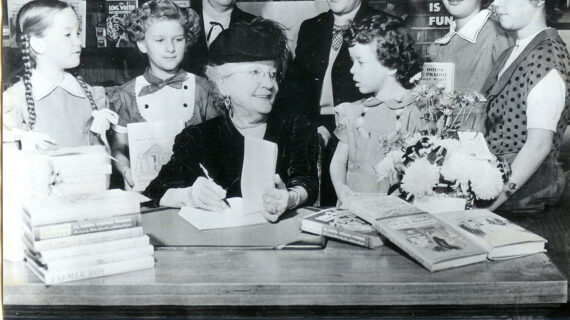 A woman author signs a book while smiling at a young girl