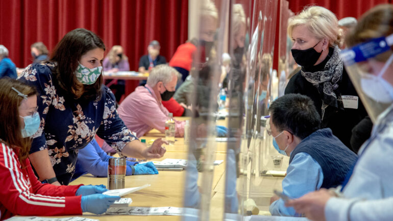 Election observers, right, look on and ask questions through plexiglass screens as officials at the Dane County recount sort through ballots by hand at the Monona Terrace in Madison, Wis., on Nov. 21, 2020. Donald Trump’s campaign is paying for a recount of votes in Dane and Milwaukee counties in an effort to identify ballots to challenge the election. (Courtesy: Will Cioci / Wisconsin Watch) Election observers, right, look on and ask questions through plexiglass screens as officials at the Dane County recount sort through ballots by hand at the Monona Terrace in Madison, Wis., on Nov. 21, 2020. Donald Trump’s campaign is paying for a recount of votes in Dane and Milwaukee counties in an effort to identify ballots to challenge the election. (Courtesy: Will Cioci / Wisconsin Watch)