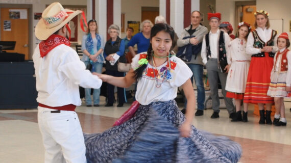 A young girl in colorful dress dances with a male partner.