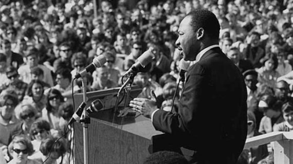 Martin Luther King Jr. stands at a podium and addresses a large crowd of people outdoors.