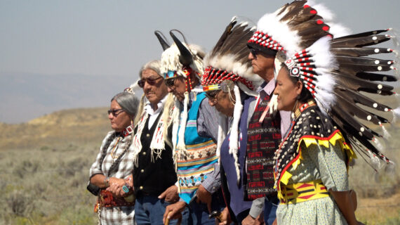 A group of Native Americans stand together. They are dressed in traditional Native American clothing and headdresses.