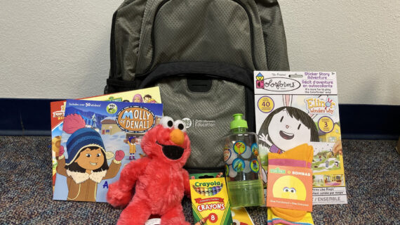 backpack against wall with books, stuffed animal, and crayons in front of it