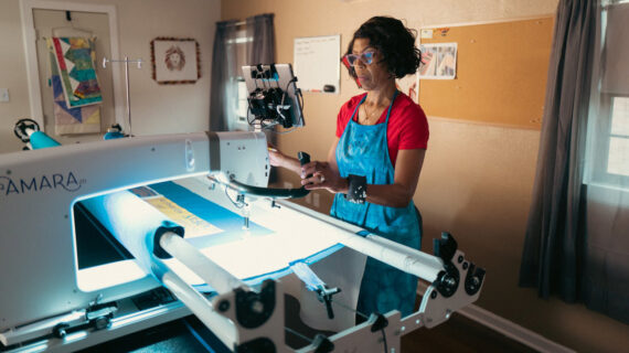 A woman stands at a longarm quilting machine.