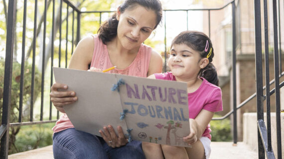 A mother and daughter side outside on their stoop. Together they're looking at a homemade nature journal.