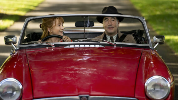 A man and woman sit next to each other in a red convertible car.