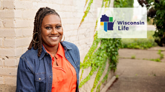 Wisconsin Life host Angela Fitzgerald standing in front of a brick building with ivy and Wisconsin Life logo in upper right-hand side.