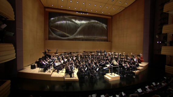 An orchestra performs in a formal musical hall.