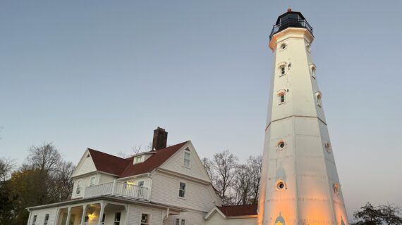 The North Point Lighthouse, a white two-story house with a burgundy roof next to a lighthouse with a tall white base capped by a burgundy top.