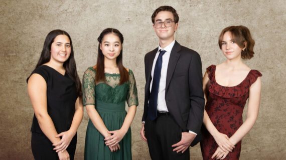 Four teenagers in formal wear smile, posing in front of a blank backdrop.