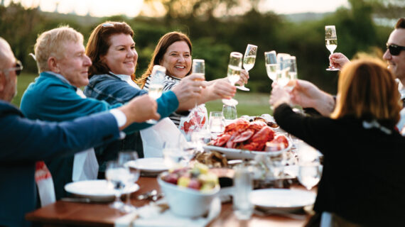 A group of diners seated at an outdoor table raise their Champagne glasses in a toast.