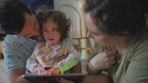 A man embraces his young daughter while the girls mother looks on.