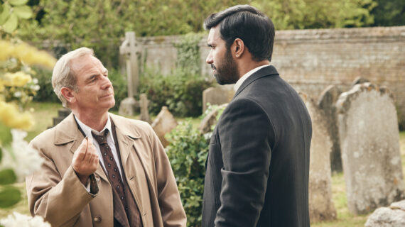 Two men standing in a graveyard have a serious conversation.