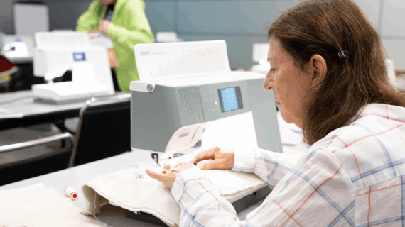A woman works at a sewing machine, an array of sewing machines are blurred beyond her scope.