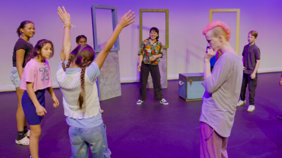 A group of children and adults play a game on a theater stage.