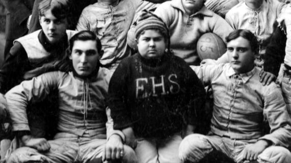 A vintage black and white photo of the Evansville High School football team. The central figure, team mascot Lloyd 