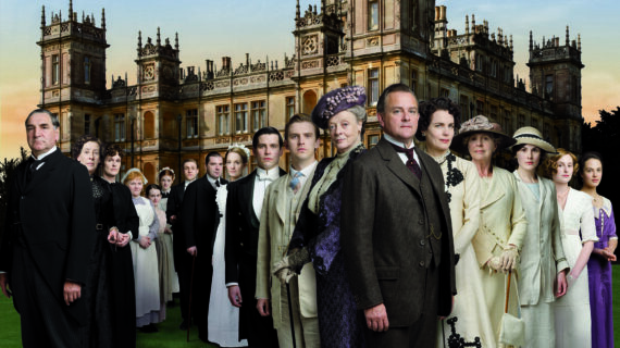 A cast of characters wearing 20th-century attire stand shoulder to shoulder against a backdrop featuring a castle.