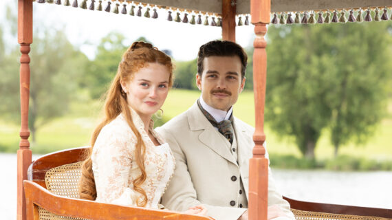 A young couple in Victorian era attire smile from beneath a carriage.