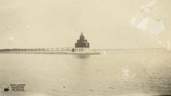 Historic black-and-white photo of the Manitowoc North Breakwater Lighthouse, 1926. Lighthouse stands solitary on calm water under an open sky, conveying serenity.