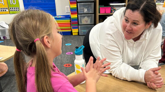 A teacher and elementary student talk at a desk