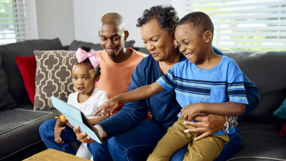A grandmother and three grandchildren play a game on a tablet.