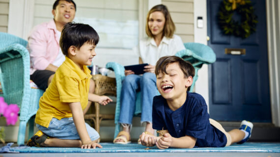 Two children smiling while on the floor playing with two adults looking on in the background.