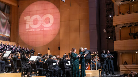 Working in concert to produce “Madison Symphony at 100” Madison Symphony Orchestra and Madison Symphony Chorus perform at the Overture Center for the Arts during the MSO's Centennial Festival Weekend concert as soloists sing beneath a “Together in Music” projection, creating a celebratory mood.